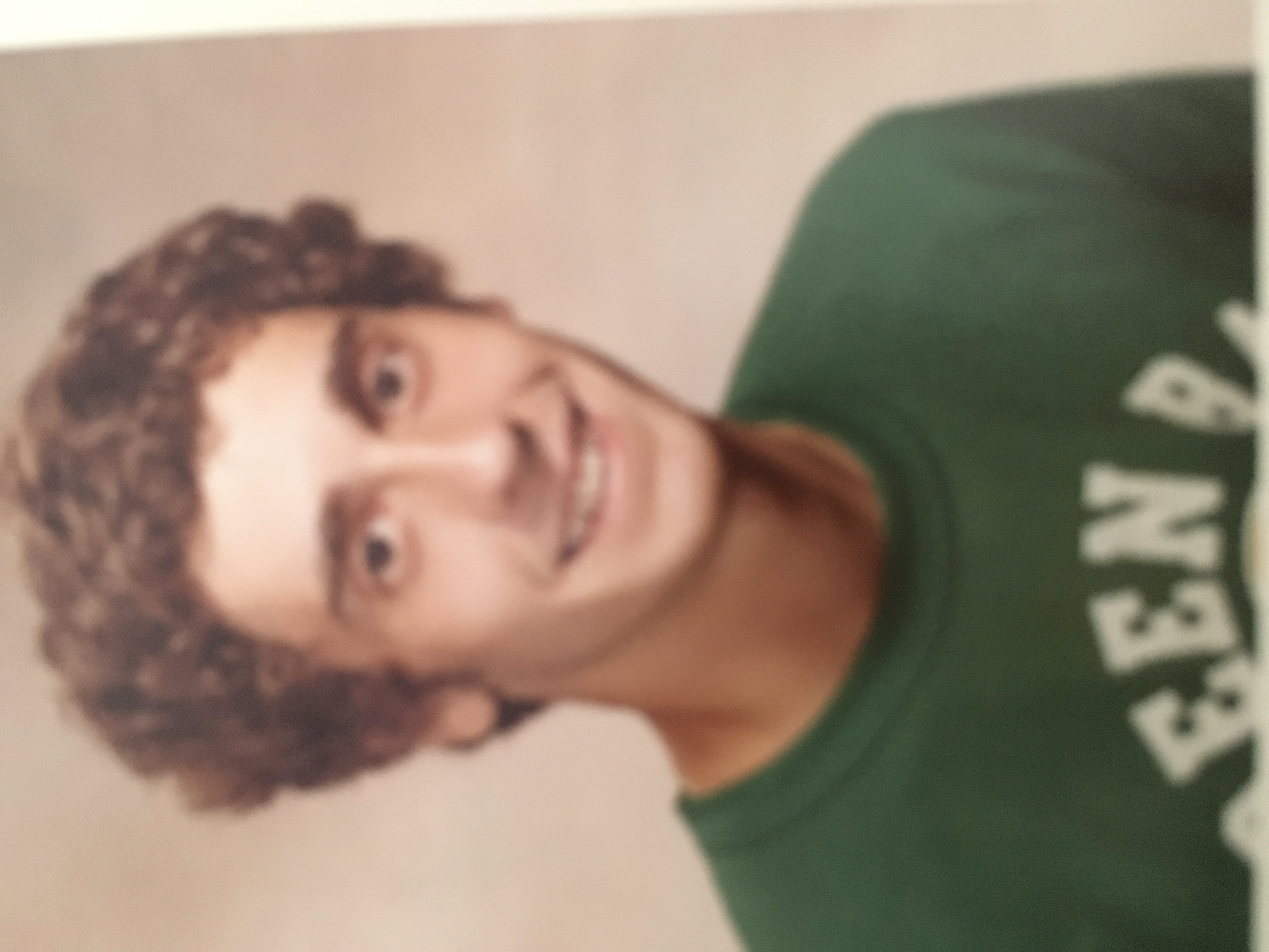 Principal as high school student wearing green sweatshirt, with brown curly hair